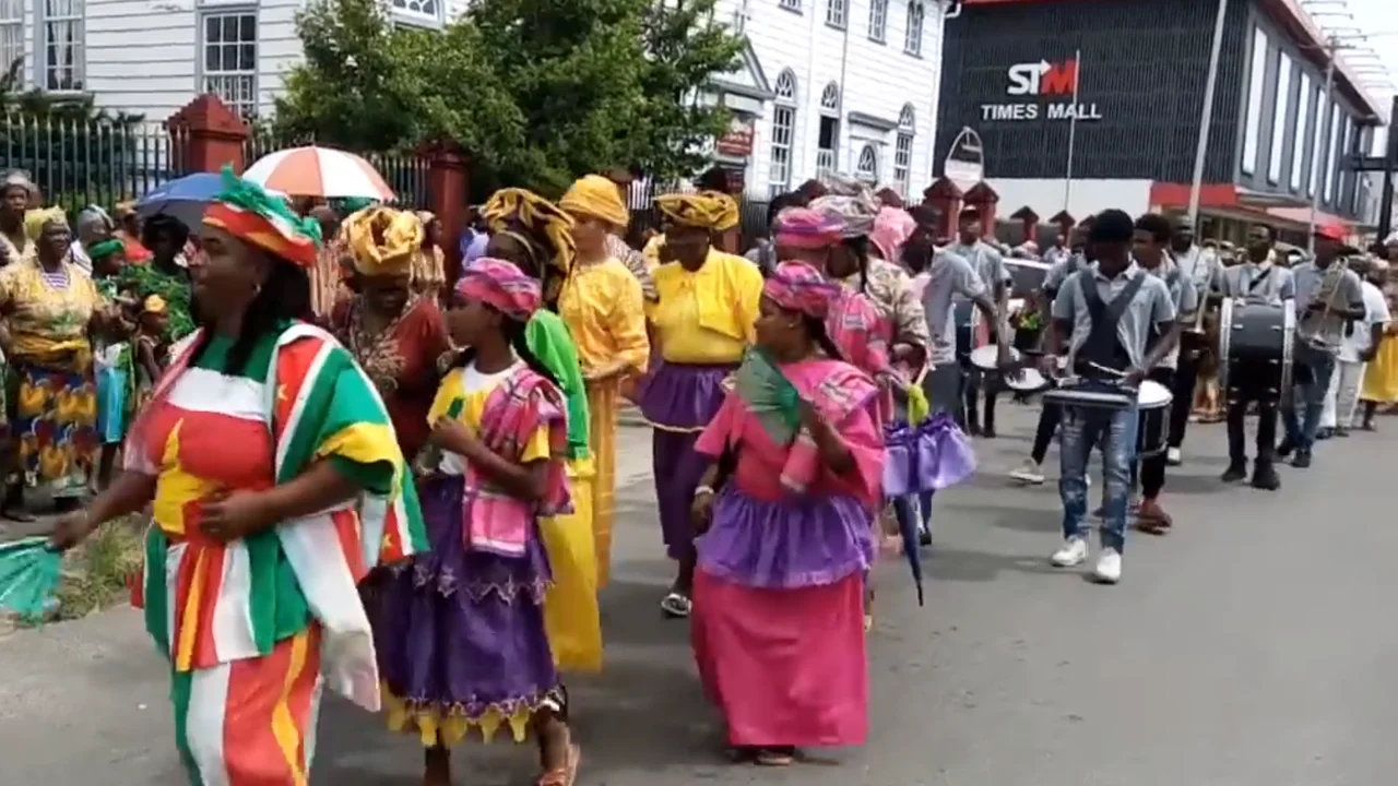 Marching brass band and participants in traditional Afro-Surinamese koto dresses during the Keti Koti Bigi Spikri parade in Paramaribo.