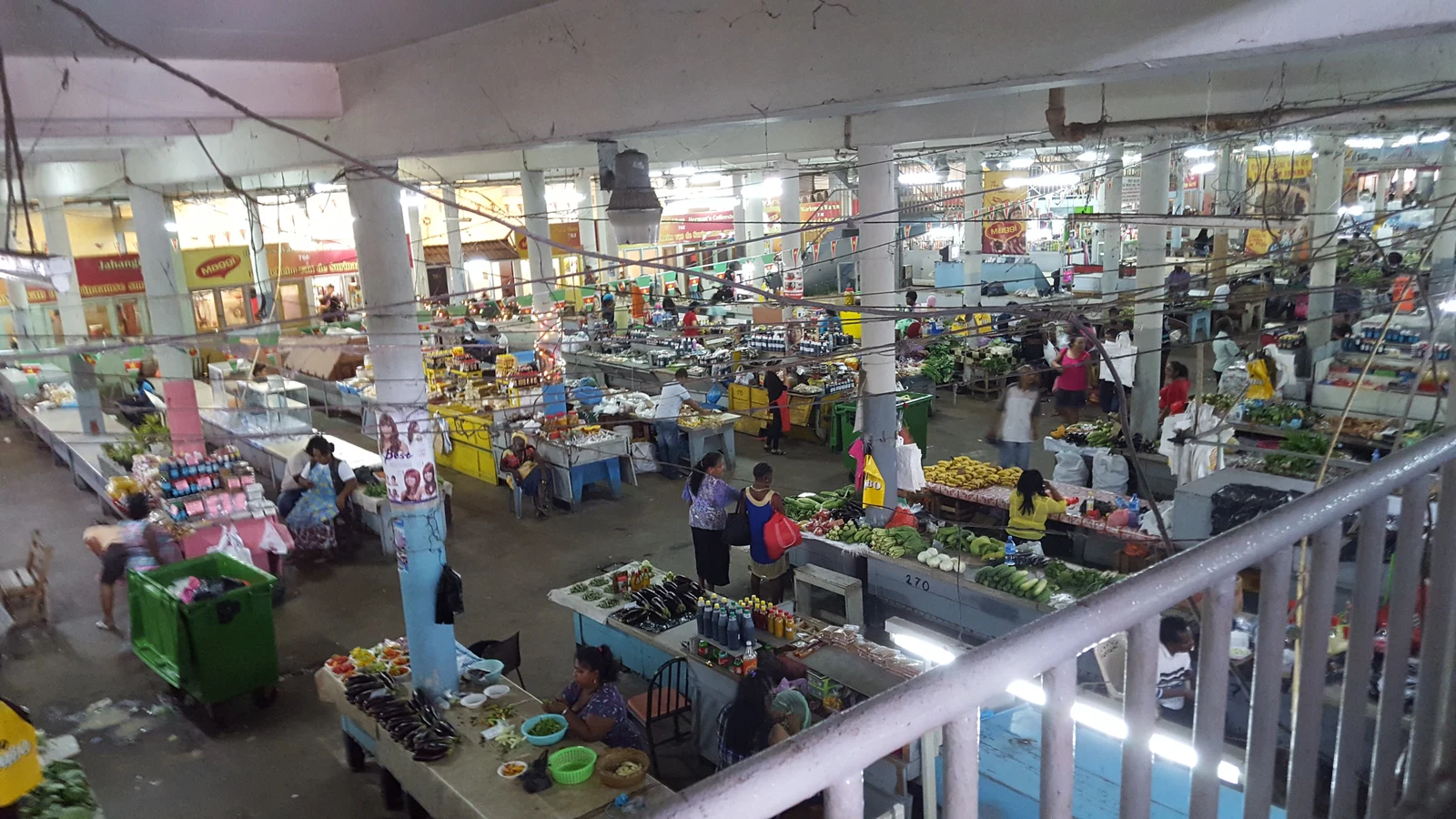 Covered ground floor aisles where market women display root vegetables, leafy greens, and spices.