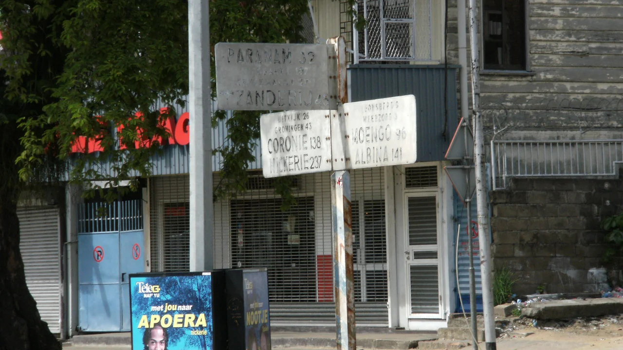 Urban street corner in Paramaribo displaying transit signs and commercial notices.
