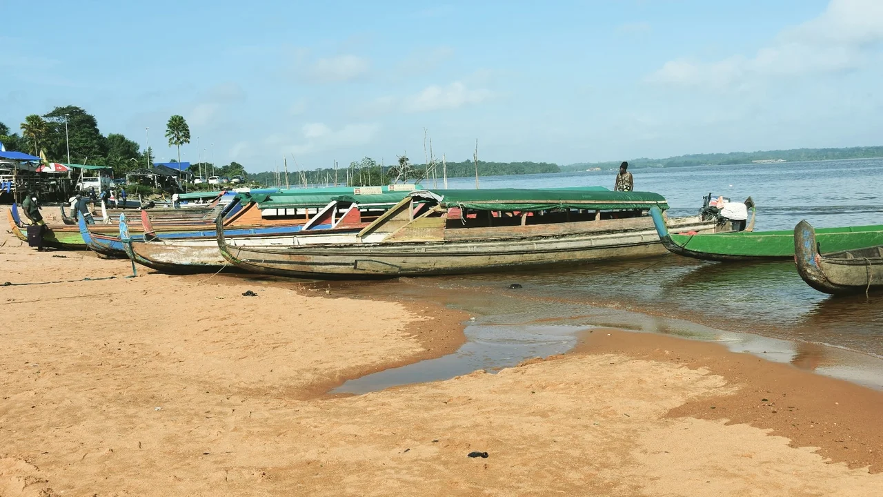 Traditional motorized wooden pirogues moored along the sandy riverbank of the Marowijne River.